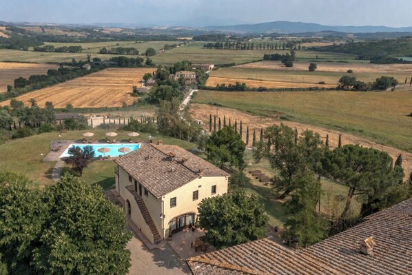 Une villa avec piscine, entourée de champs et d’arbres.