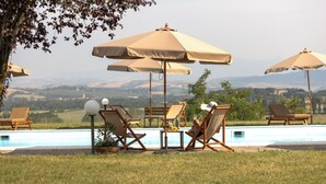 Area piscina con sedie a sdraio e ombrelloni, con vista su un paesaggio suggestivo.