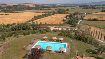 A pool area with lounge chairs and umbrellas, surrounded by a rural landscape with fields and trees.