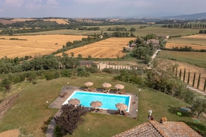A pool area with lounge chairs and umbrellas, surrounded by a rural landscape with fields and trees. - Villa Comunello (Monteroni d'Arbia SI)