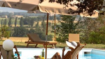 Un área junto a la piscina con sillones de descanso, una mesa con una bebida y vistas al campo.