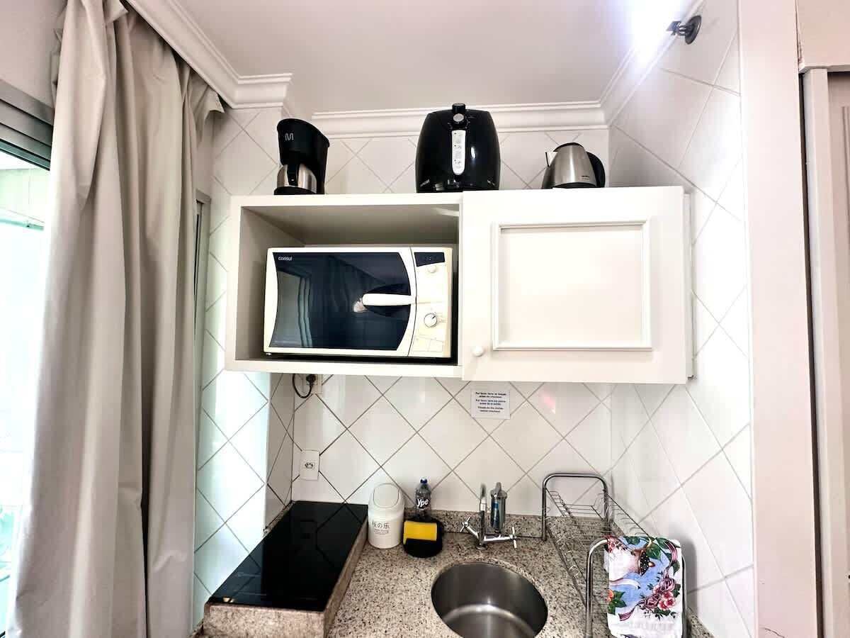 Een kleine keuken met een magnetron, waterkoker en koffiezetapparaat op een witte kast.
