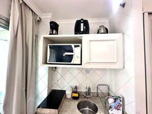 Una kitchenette compacta con microondas, hervidor de agua y cafetera sobre un mueble blanco.