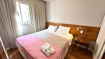 Een hotelkamer met een bed, nachtkastje, lamp en een raam met gordijnen.