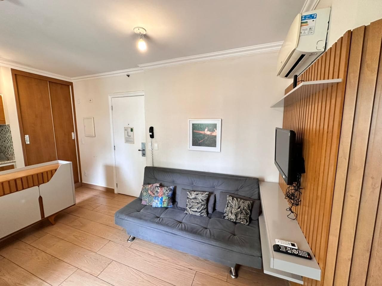 Un salon avec un canapé gris, un téléviseur fixé à un mur en bois et un meuble blanc doté d’un plan de travail en bois.