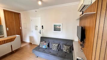 Un salon avec un canapé gris, un téléviseur fixé à un mur en bois et un meuble blanc doté d’un plan de travail en bois.