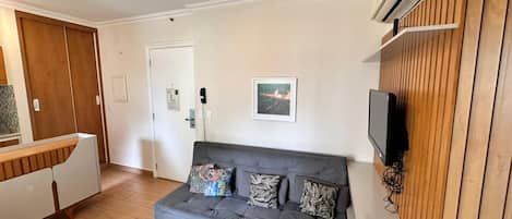 A living room with a grey sofa, a television mounted on a wooden wall, and a white cabinet with a wooden countertop.