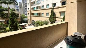 Un balcon avec une chaise, une poubelle et une vue sur un immeuble de grande hauteur, doté de nombreux étages et balcons.