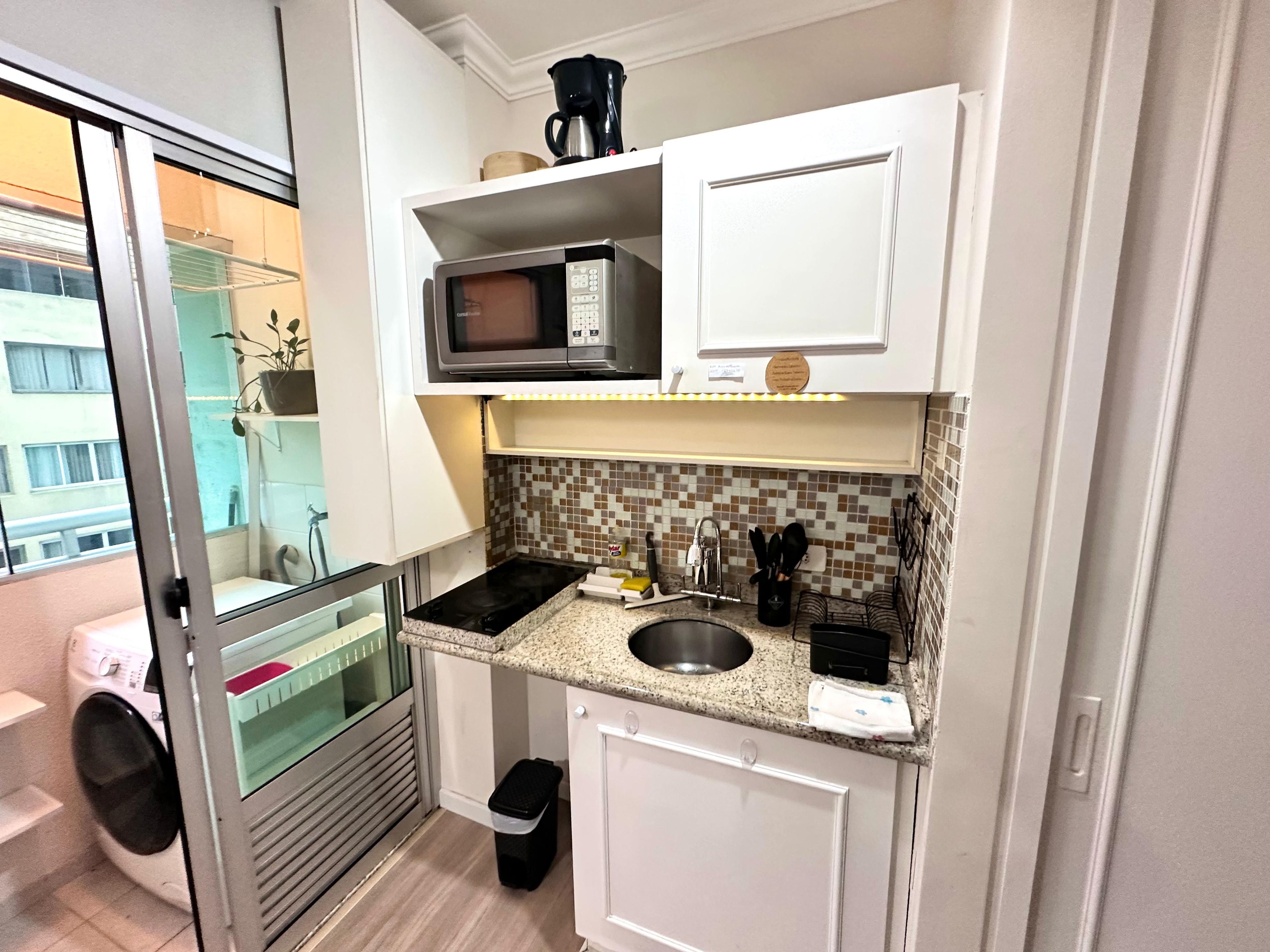 A compact kitchen with a microwave, sink, and a small trash bin.