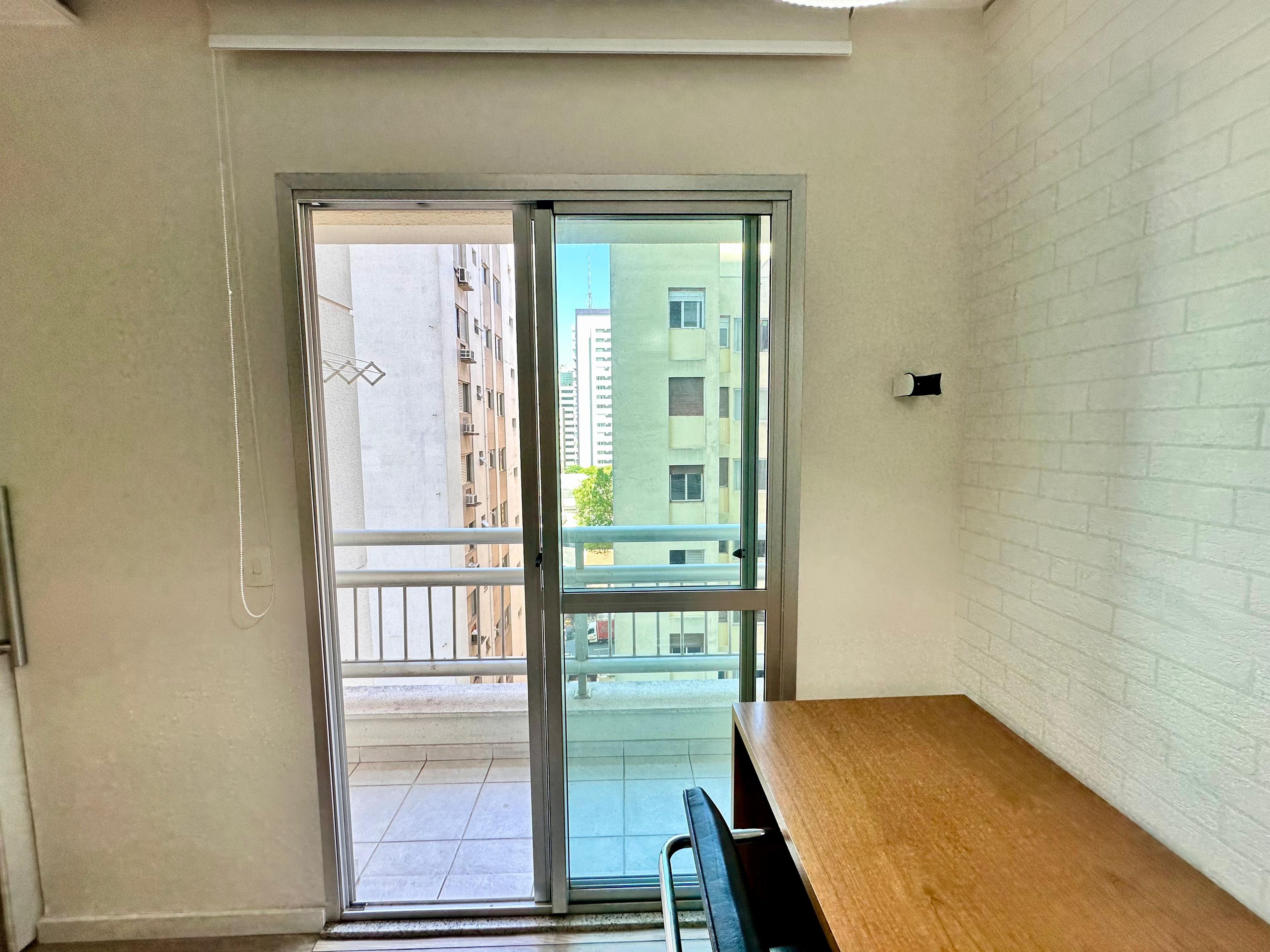 Une pièce avec une table en bois, une porte-fenêtre coulissante donnant sur un balcon et un mur en briques blanches.