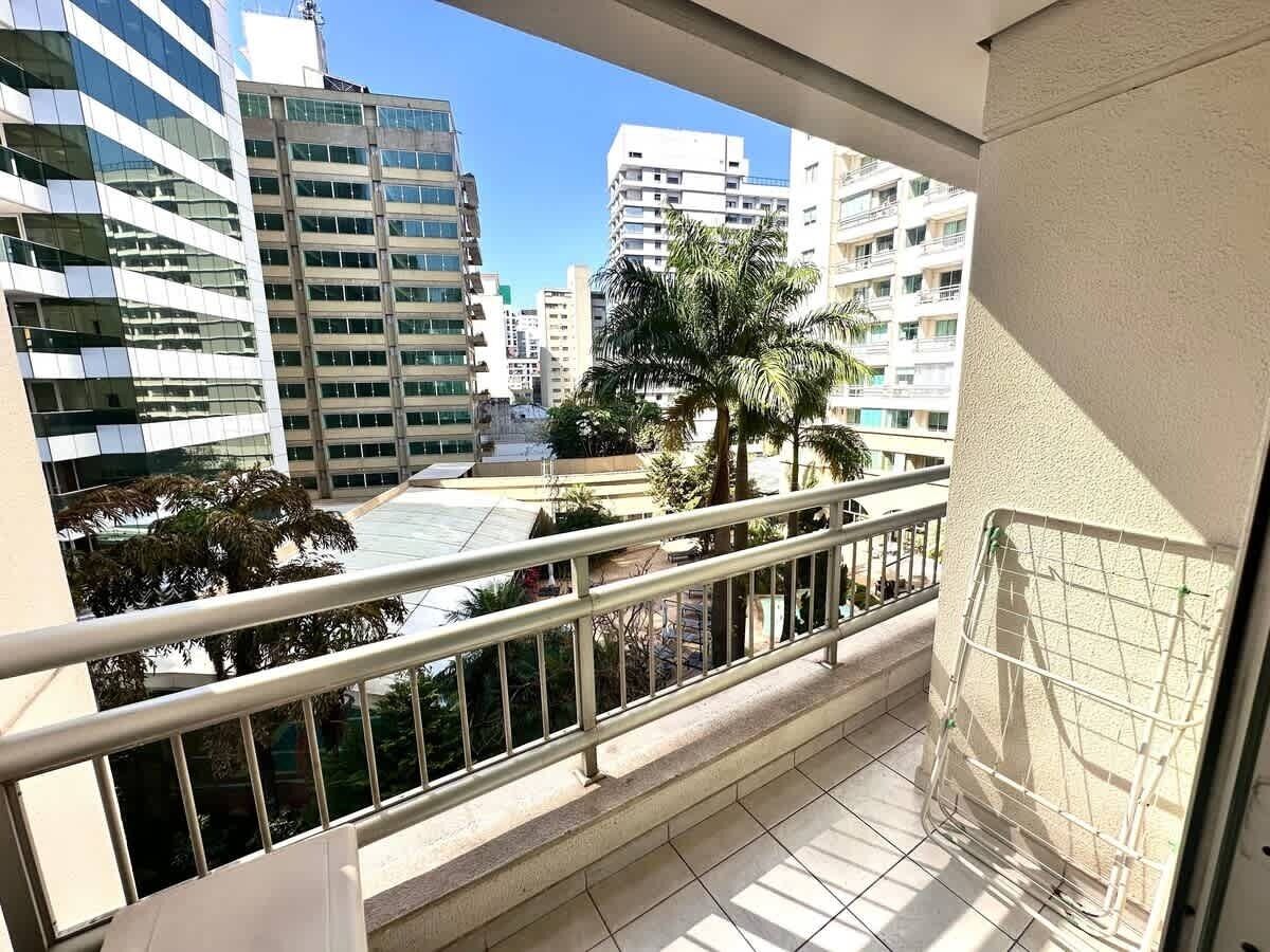 Een balkon met een metalen hekwerk, uitzicht op hoge gebouwen en een palmboom.