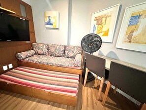 Ein Zimmer mit einer Couch, einem Ventilator, einem Fernseher und Bildern an den Wänden.
