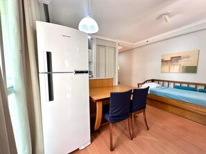 Una habitación compacta con kitchenette, una mesa de comedor con sillas, una cama y un ventilador de techo.