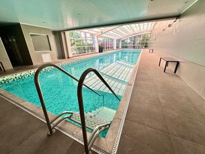 Una piscina interior con agua cristalina, solárium con baldosas y techo de cristal.