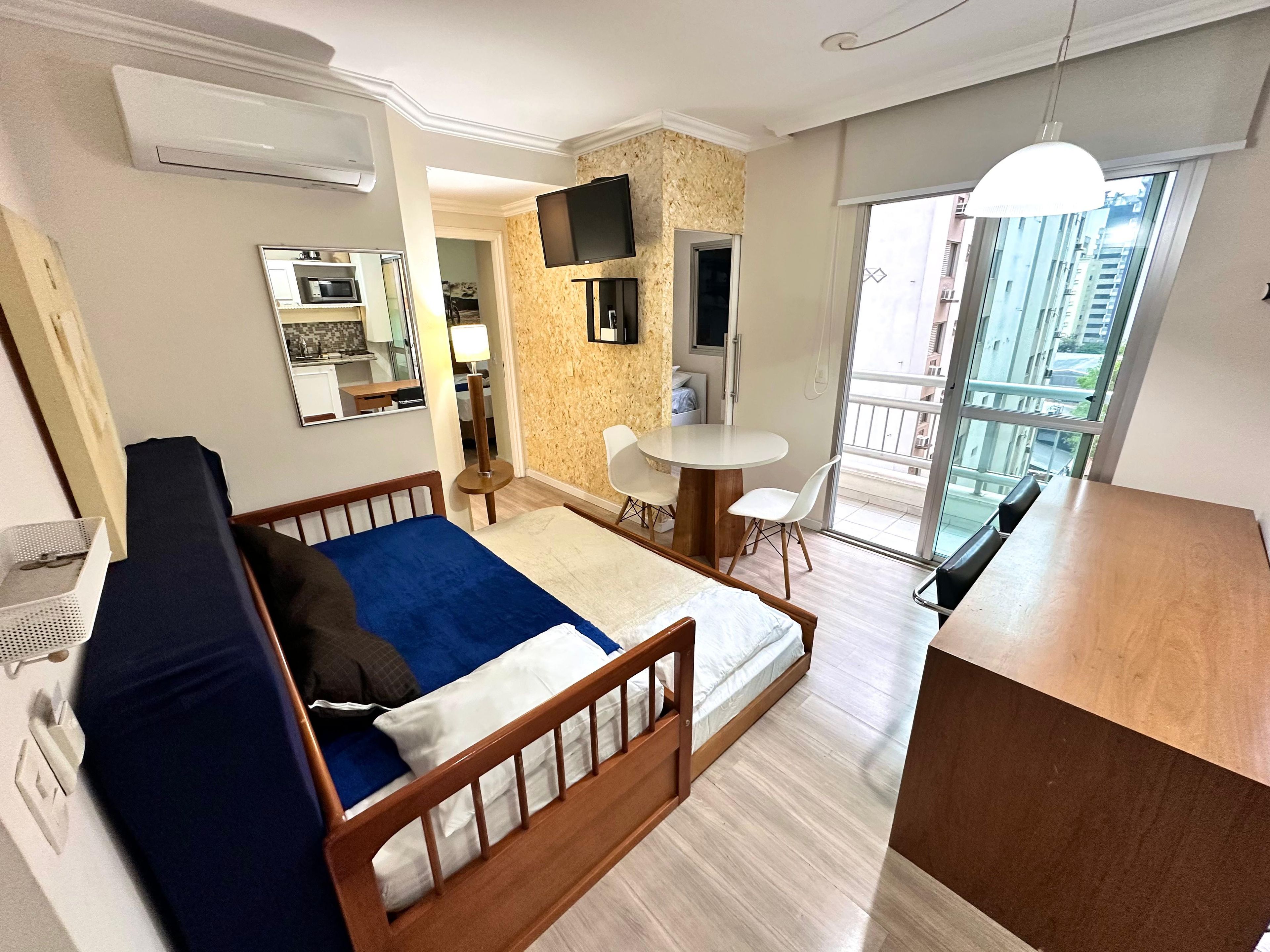 Un dormitorio con cama, escritorio, silla, televisor y balcón con vistas.