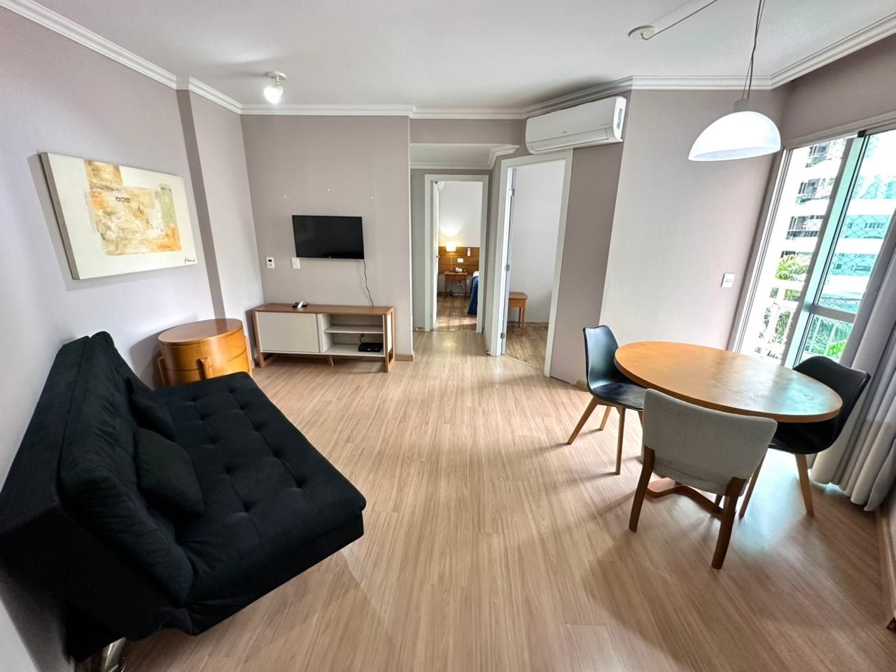 Ein modernes Wohnzimmer mit Sofa, Esstisch mit Stühlen, Fernseher und einem Flur, der in einen weiteren Raum führt.