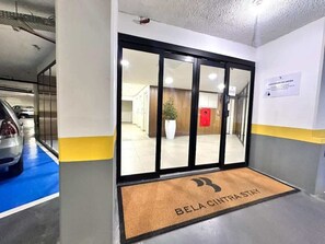 Entrada de hotel con felpudo, mostrador de recepción y zona de estacionamiento con un tapete azul.