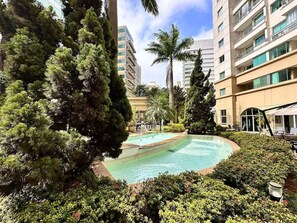Una piscina rodeada de abundante vegetación y edificios modernos.
