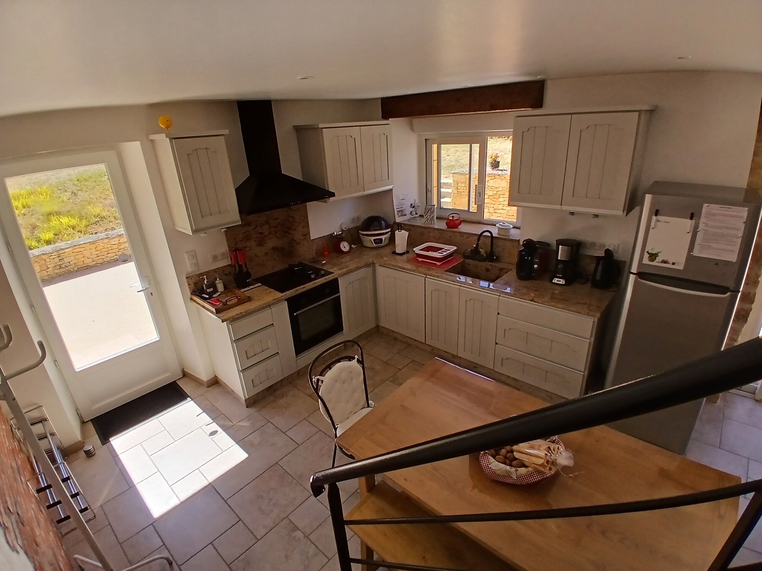 A kitchen with a central island, a stove, and a sink. There is a window above the sink and a door leading outside.
