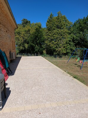 A paved outdoor area with a playground and a building with a stone facade. - L'Establou Farm Stay (COLY ST AMAND)