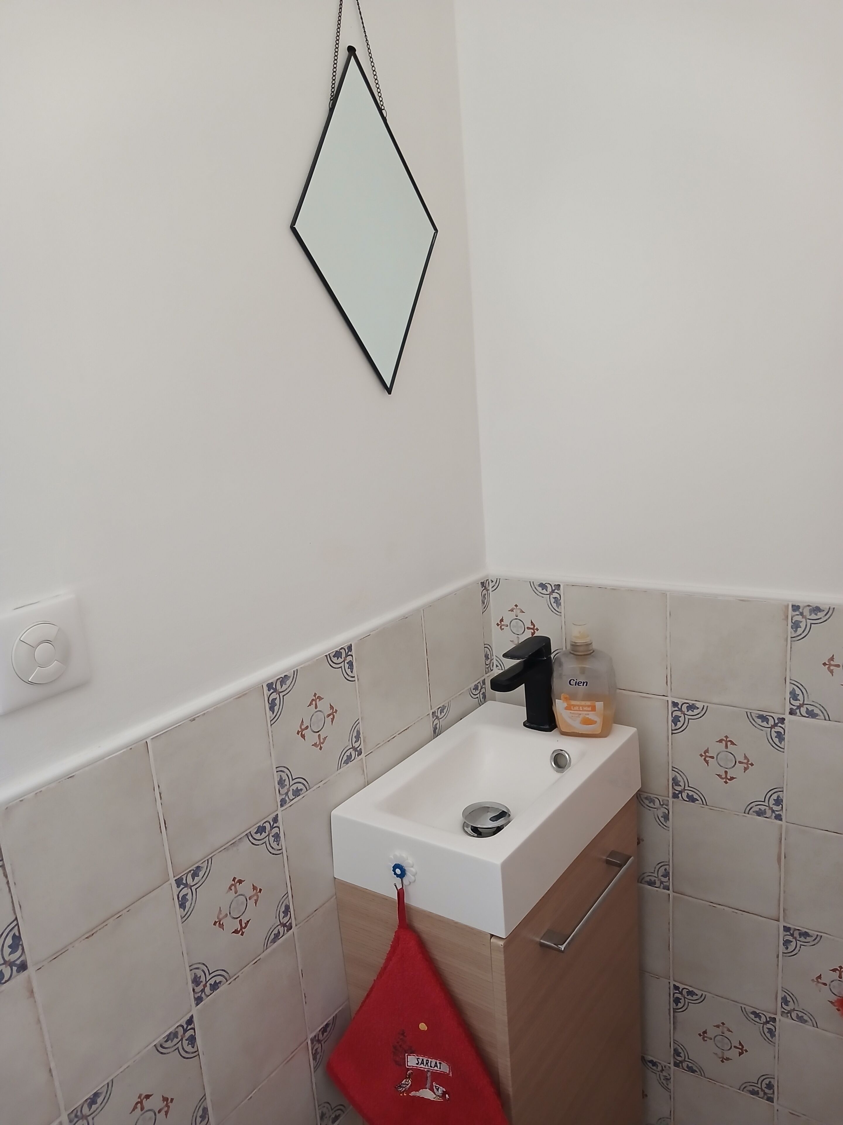 Une salle de bain avec un lavabo blanc, un miroir et des carreaux à motifs.