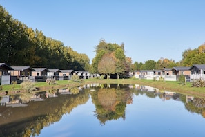 Eine Reihe von Hütten mit einem Teich im Vordergrund, der die Gebäude und Bäume spiegelt.
