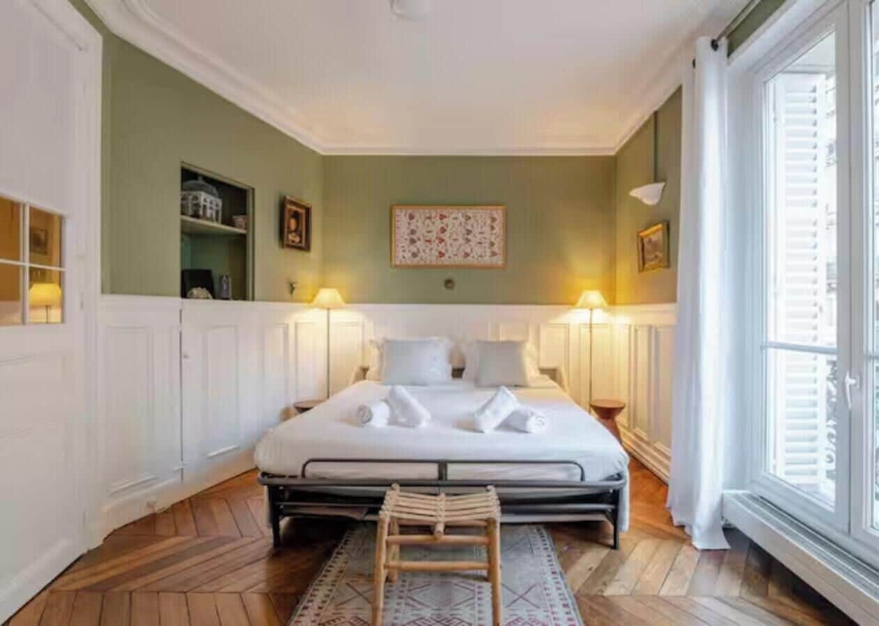 Ein Hotelzimmer mit einem großen Bett, Nachttischlampen, Holzboden und einem Fenster mit Jalousien.