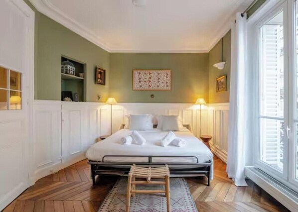 A hotel room with a large bed, bedside lamps, a wooden floor, and a window with blinds. - COMBINATION OF PARISIAN ARCHITECTURE WITH MODERN COMFORT - RUE DE RENNES (Paris)