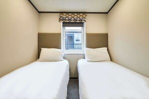 Una habitación de hotel pequeña y estrecha con dos camas individuales, una ventana con cortina decorativa y vistas al exterior.