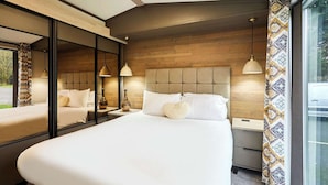 Una habitación de hotel con una cama grande, mesitas de noche, un espejo y una ventana con cortinas.