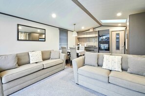 Ein modernes Wohnzimmer mit zwei Sofas, einem Esstisch und einer Küchenzeile inklusive Backofen und Fenster.