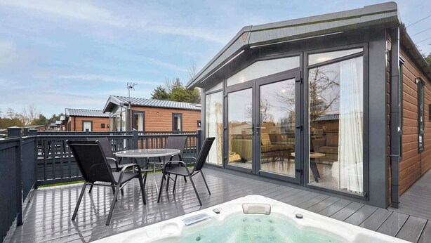 Un jacuzzi en una terraza de madera con un porche acristalado.