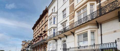 Una hilera de casas adosadas tradicionales con balcones, una calle pavimentada y coches aparcados.