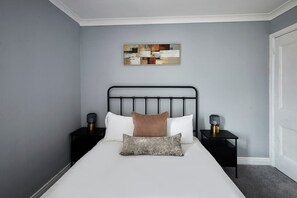 Een slaapkamer met een bed, twee nachtkastjes, een schilderij en een deur.