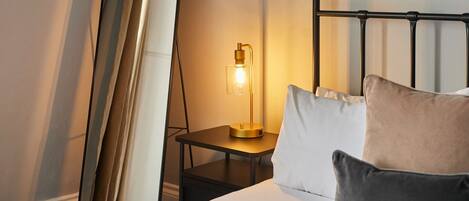 Una habitación de hotel con una cama, almohadas, una mesita de noche, una lámpara y un espejo.