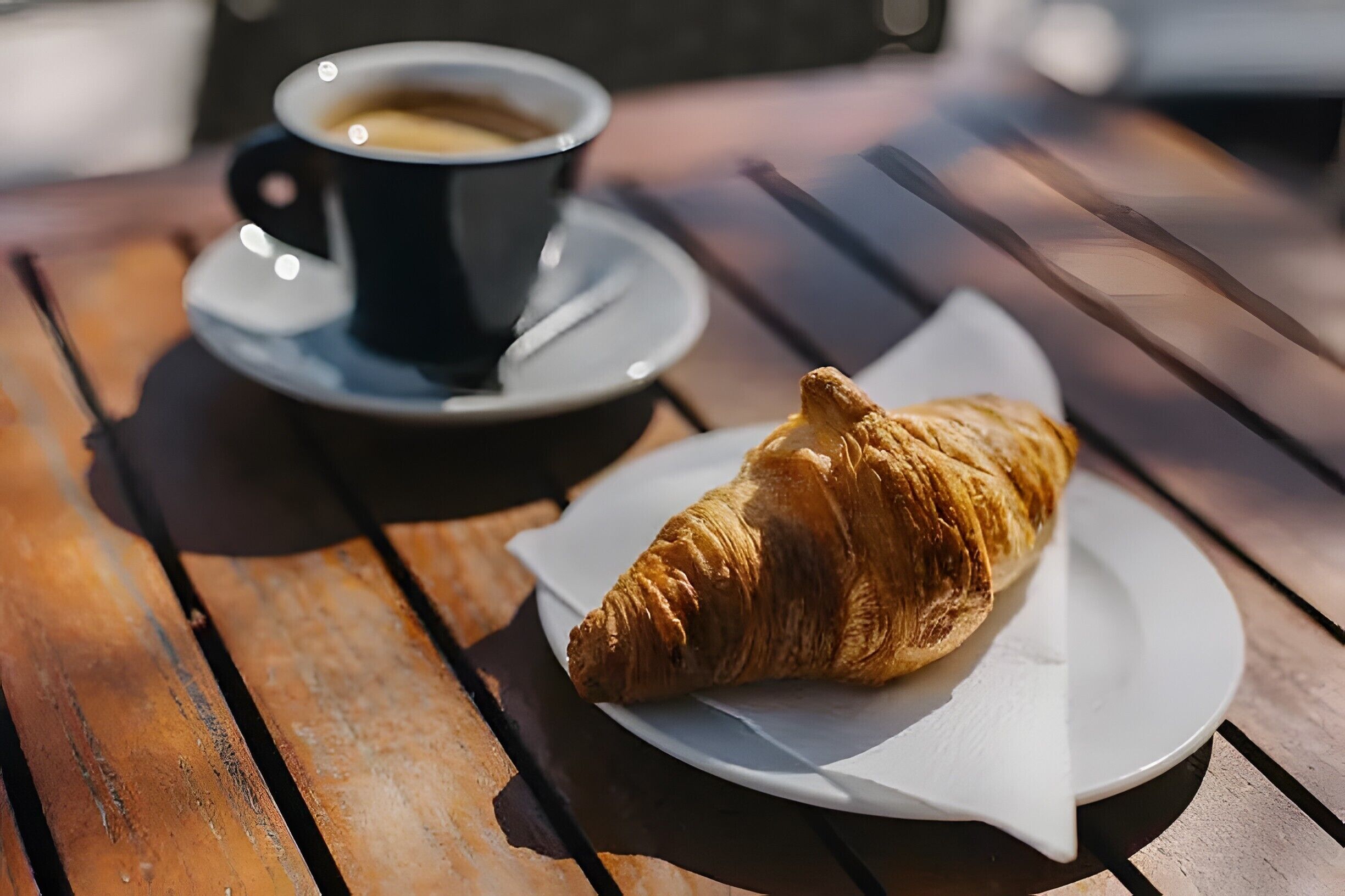 Une table en bois sur laquelle se trouvent un croissant et une tasse de café posée sur une soucoupe.