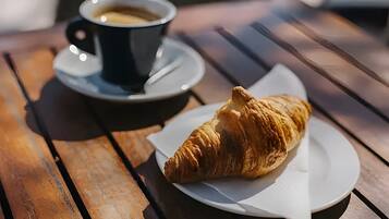 Une table en bois sur laquelle se trouvent un croissant et une tasse de café posée sur une soucoupe.