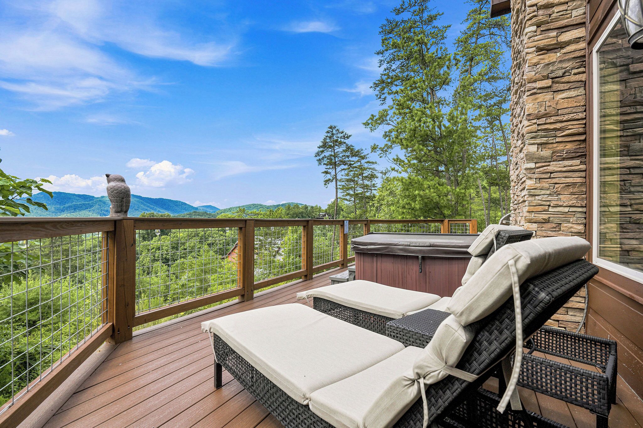 A deck with two lounge chairs and a hot tub, overlooking a mountainous landscape.