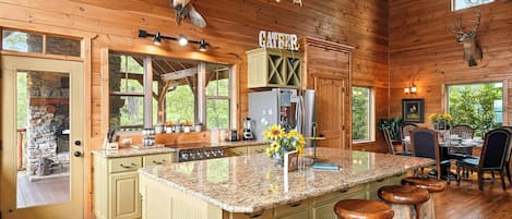 L’intérieur d’une cabane comprend un îlot de cuisine, des tabourets de bar, un coin repas et une cheminée en pierre.