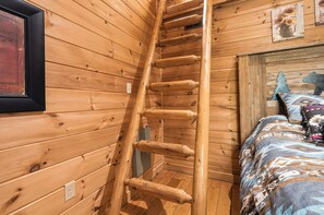Ein Holzinnenraum mit einer Wendeltreppe, einem Bett mit gemusterten Betttextilien und einem gerahmten Bild an der Wand.