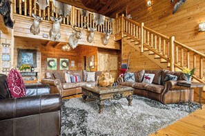 Ein rustikales Holzhäuschen im Inneren mit einer Holztreppe, Ledersofas und Hirschgeweihen an den Wänden.