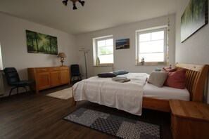 Une chambre à coucher comprenant un lit, un bureau, une chaise, une armoire et deux fenêtres.