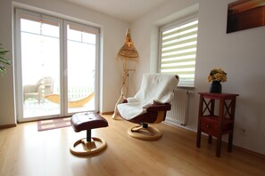 A room with a wooden floor, a white chair with a towel, a small wooden table with a vase, and a window with blinds. - Appartement im Seedomizil Kummerow (Kummerow)