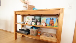 Ein Holzregal mit verschiedenen Kinderspielzeugen und -spielen, darunter Knobelkästchen und einer Spielmaus.