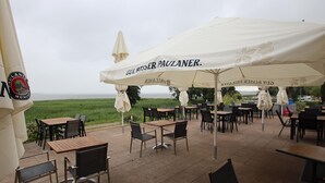 Ein Außenbereich mit Tischen und Stühlen unter Sonnenschirmen mit Blick auf ein Gewässer.