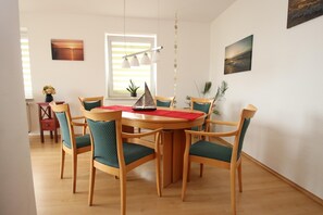 A dining area with a round wooden table, six chairs with green upholstery, a red placemat, and a decorative metal sculpture. - Appartement im Seedomizil Kummerow (Kummerow)