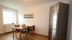 Eine kleine Küche mit Esstisch, Stühlen, einem Kühlschrank und einem Fenster.