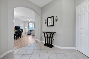A hallway with a dining area, a table with chairs, a black console table, and a white door. - Beautiful Vista Cay Condo Next to Clubhouse - 3033 (Orlando)