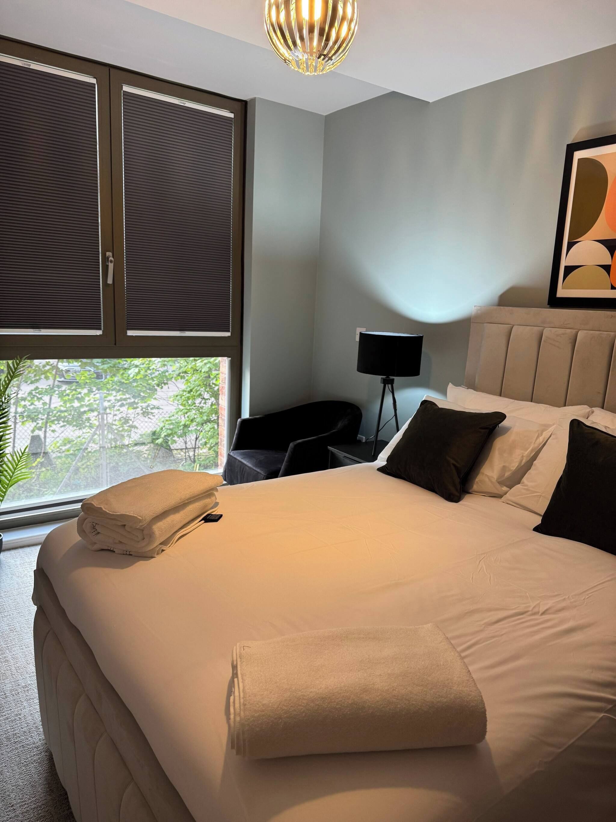 Una habitación de hotel con una cama grande, una mesita de noche, una lámpara y una ventana con persianas.