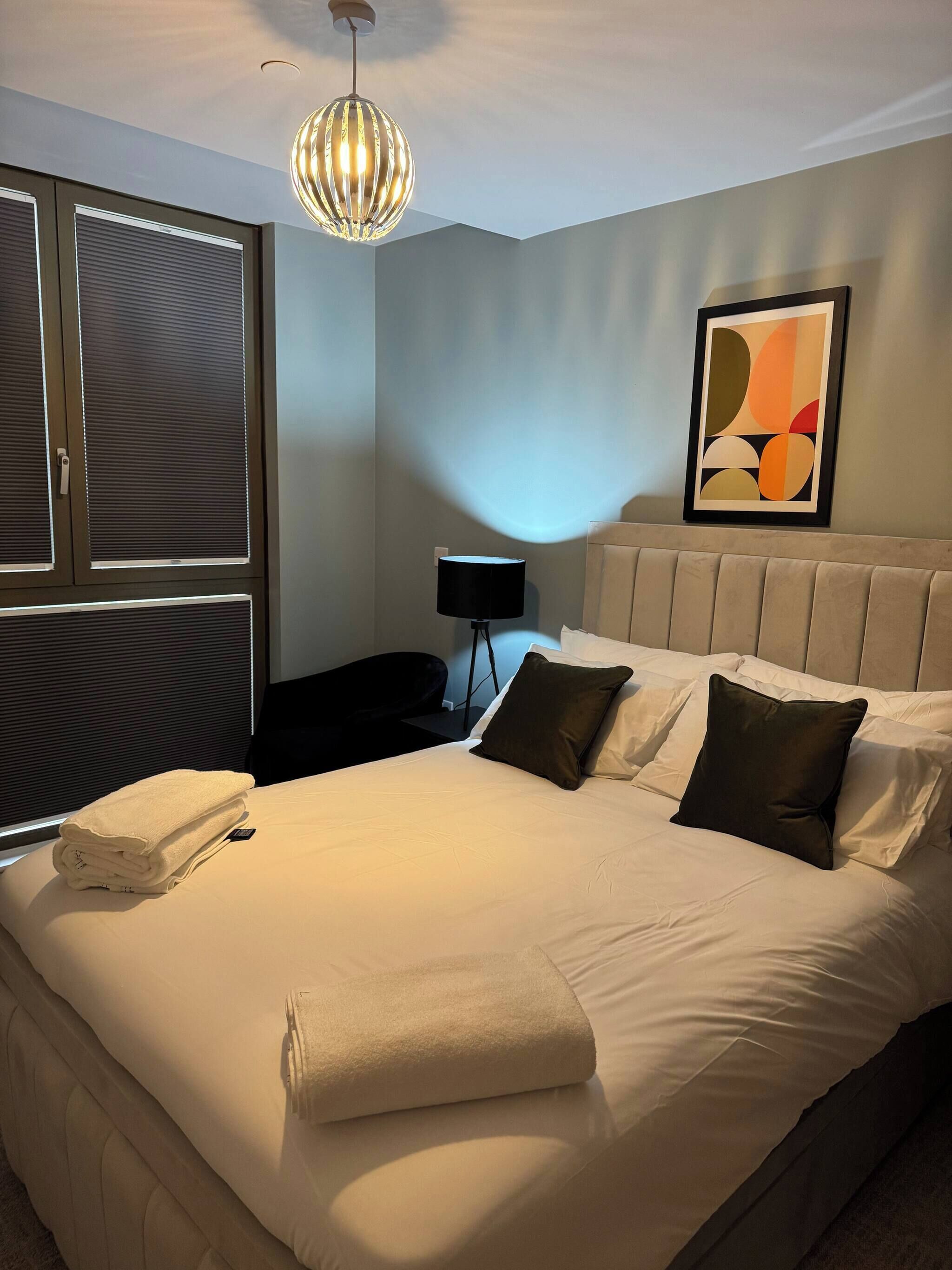 Een hotelkamer met een bed, een bedlamp, een raam met zonwering en een plafondlamp.